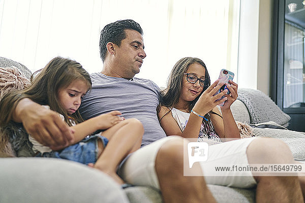 Vater beobachtet Töchter beim Spielen von Computerspielen auf dem Handy