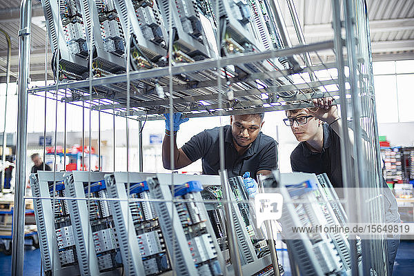 Workers with electronic parts on racks in electronics assembly factory