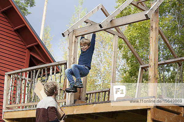 Father watching boy swinging on beam of unfinished treehouse