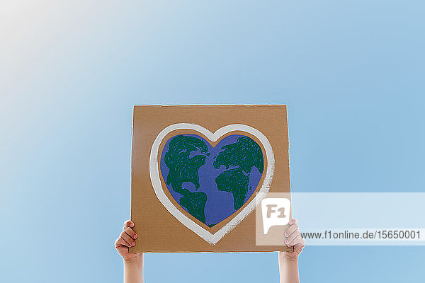 Young environmental activist holding sign against blue sky