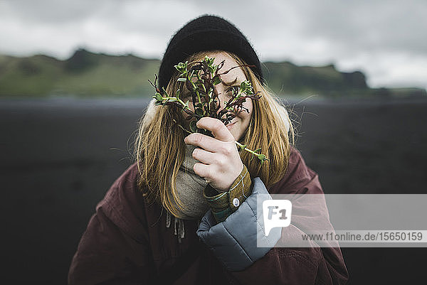 Frau hält Pflanzen über ihr Gesicht am Strand