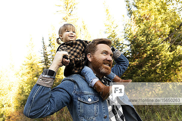Vater trägt seine Tochter auf den Schultern im Wald
