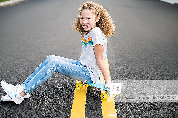 Girl sitting on skateboard on road