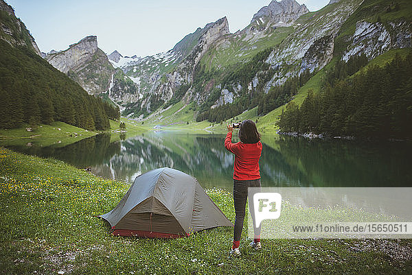Woman taking photograph by tent near Seealpsee lake in Appenzell Alps  Switzerland