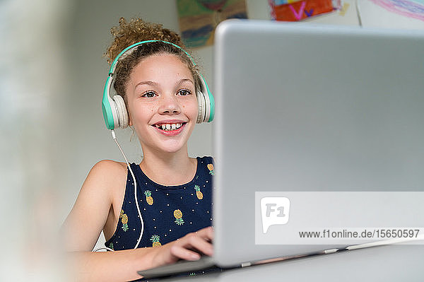 Smiling girl wearing headphones using laptop