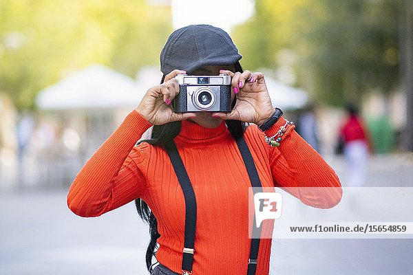 Beautiful young woman with dark skin making a photograph with an old vintage type photo cmara.