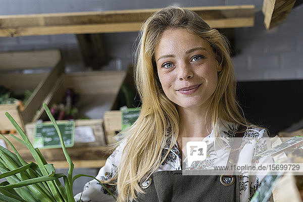 Lächelnde junge Frau hält Frühlingszwiebel in Weidenkorb