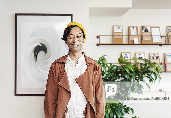 Männlicher japanischer Profi  der in einem Arbeitsraum steht und in die Kamera lächelt.