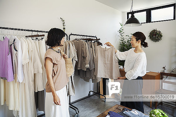 Zwei Japanerinnen stehen in einer kleinen Modeboutique und schauen auf Oberteile.