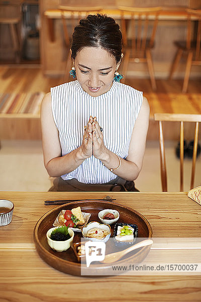 Schrägaufnahme einer Japanerin  die in einem Café vor einer Auswahl vegetarischer Speisen sitzt.