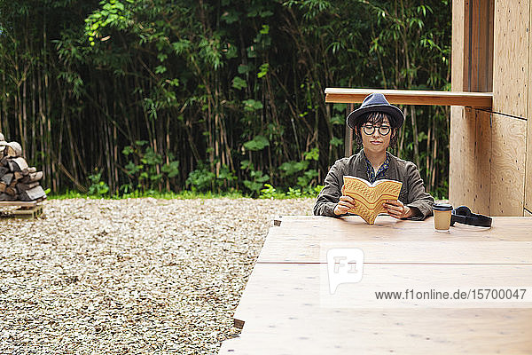 Japanerin mit Brille und Hut sitzt an einem Tisch vor dem Eco Cafe und liest ein Buch.