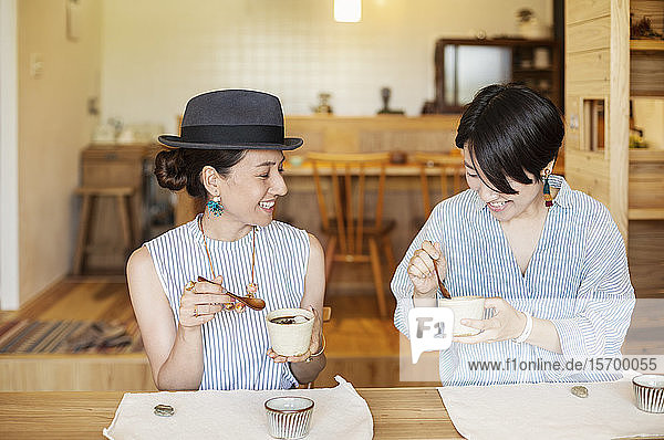 Two smiling Japanese women eating in a vegetarian cafe.