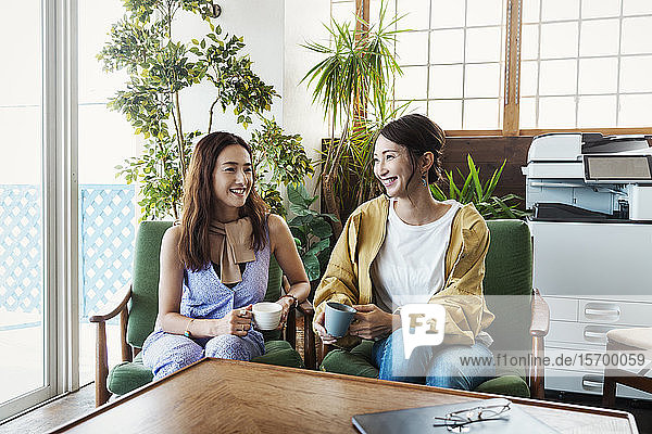 Zwei japanische Fachfrauen sitzen in einem Arbeitsraum und lächeln sich an.