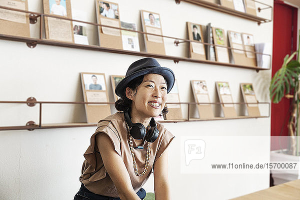 Japanische Fachfrau mit Trilby-Hut und Kopfhörern sitzt in einem Raum für Zusammenarbeit.