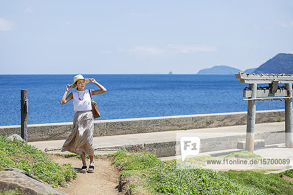 Japanische Frau mit Hut beim Spaziergang auf dem Weg am Meer.