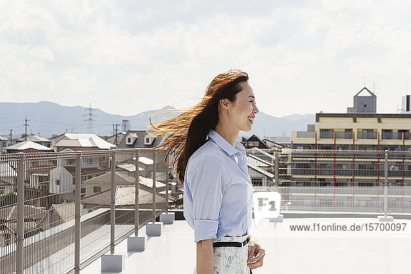 Lächelnde Japanerin  die auf einem Dach in einer städtischen Umgebung steht.