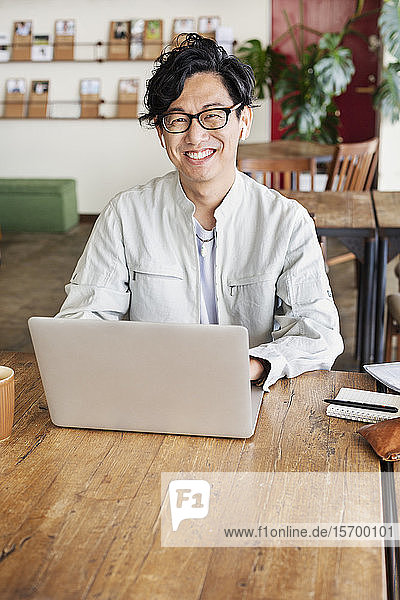 Male Japanese professional sitting at a table in a co-working space  using laptop computer.