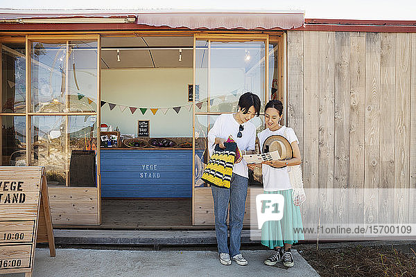 Zwei lächelnde Japanerinnen stehen vor einem Bauernladen.