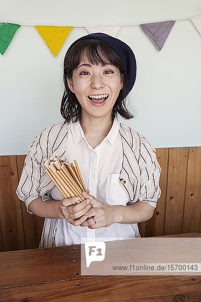Japanische Frau  die in einem Hofladen hinter der Ladentheke steht und in die Kamera lächelt.