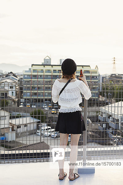 Rückansicht einer jungen Japanerin  die auf einem Dach in einer städtischen Umgebung steht.