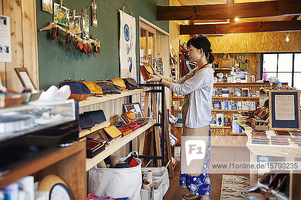 Japanerin mit Schürze  die in einem Ledergeschäft steht und eine Clutch Bag aus hellbraunem Leder hält.