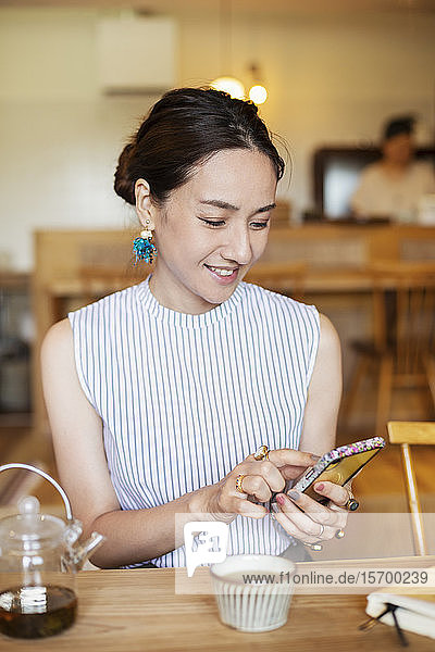 Japanerin  die an einem Tisch in einem vegetarischen Café sitzt und ein Mobiltelefon benutzt.
