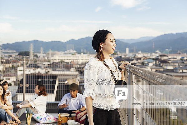 Lächelnde junge Japanerin  die auf einem Dach in einer städtischen Umgebung steht.