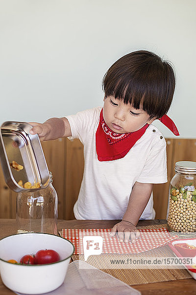 Japanischer Junge  der an einem Tisch in einem Hofladen steht und bei der Zubereitung von Essen hilft.