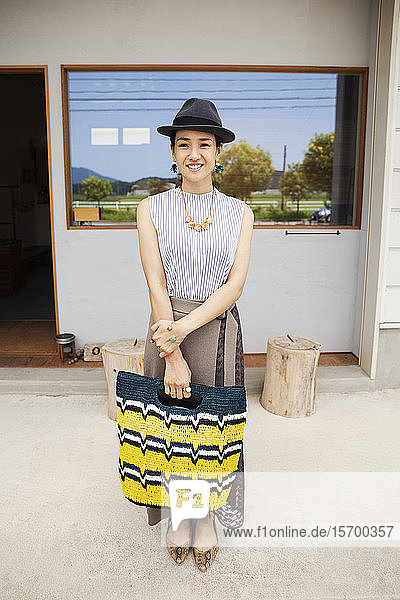 Porträt einer lächelnden Japanerin mit Hut und Einkaufstasche  die in die Kamera schaut.