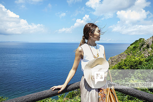 Japanese woman standing on a cliff ocean in the background.