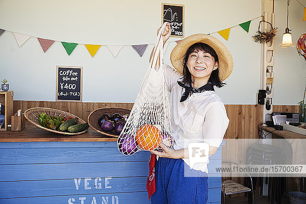 Japanische Frau mit Hut  die in einem Hofladen arbeitet und in die Kamera lächelt.