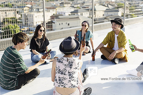 Smiling group of young Japanese men and women sitting on a rooftop in an urban setting.