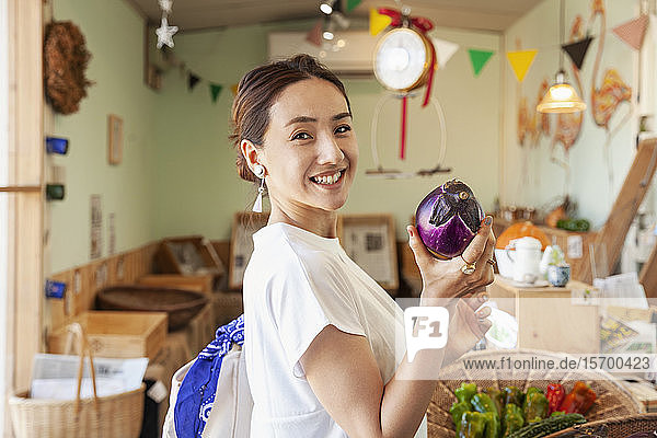 Zwei lächelnde Japanerinnen stehen in einem Bauernladen  halten Aubergine in der Hand und schauen in die Kamera.