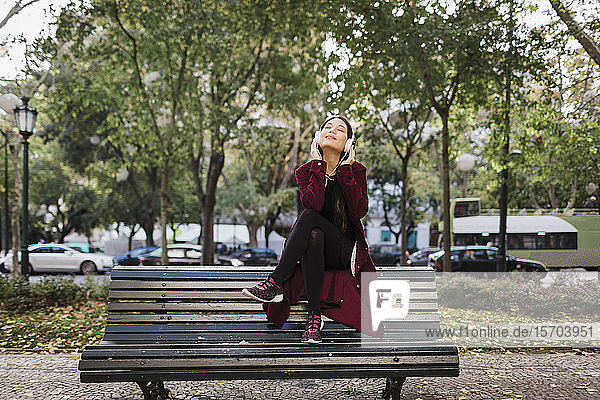 Unbekümmerte Frau  die auf einer Parkbank mit Kopfhörern Musik hört