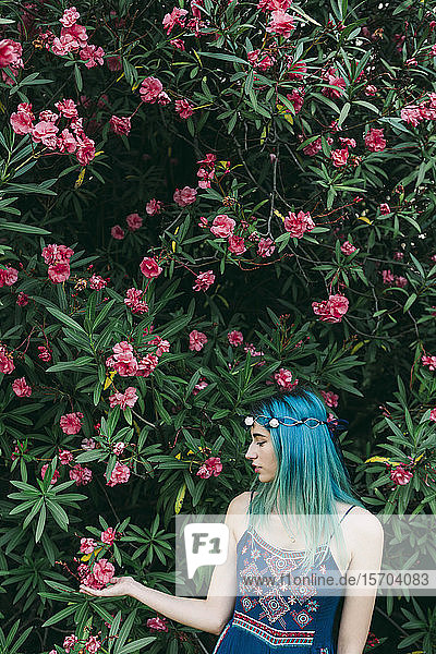 Gelassene junge Frau mit blauem Haar unter einem blühenden Baum stehend