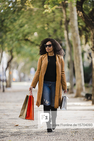 Stilvolle junge Frau mit Einkaufstaschen auf dem Gehweg
