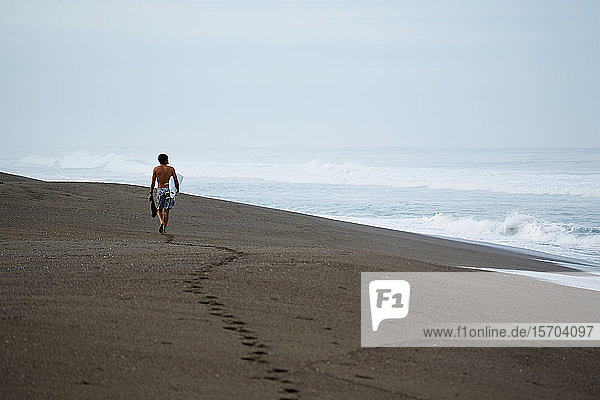 Male surfer walking with surfboard on wet sand beach
