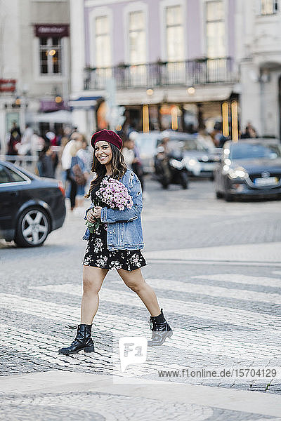 Portrait lächelnde junge Frau beim Überqueren der Straße mit Blumenstrauß