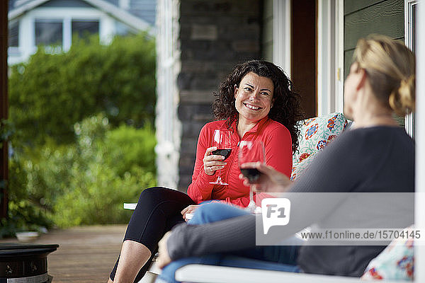 Glückliche Frauen unterhalten sich und trinken Rotwein auf der Veranda