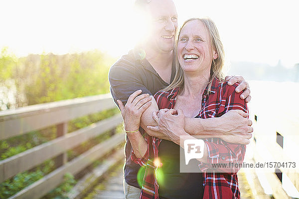 Portrait glückliches  zärtliches Paar  das sich auf einem sonnigen Sommersteg umarmt