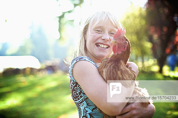 Porträt glückliches Mädchen hält Henne in sonnigen Hof