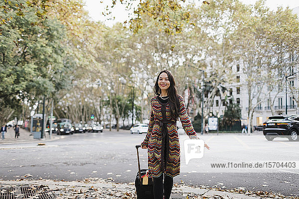 Porträt glücklicher weiblicher Tourist mit Koffer auf städtischer Herbststraße