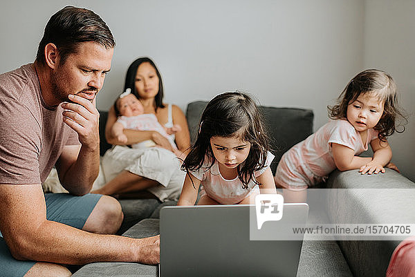 Family of five relaxing and using laptop on couch in living room