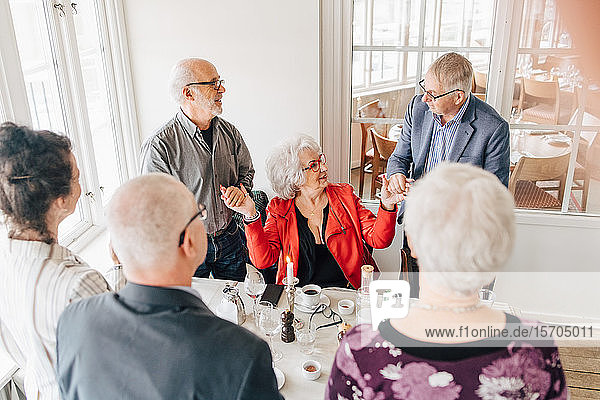Ältere Männer halten mit älterer Frau Händchen  während Freunde im Restaurant am Tisch stehen