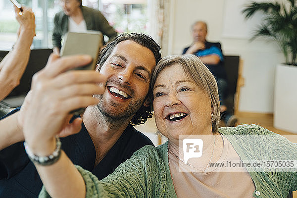 Lächelnde ältere Frau  die mit einem männlichen Mitarbeiter im Gesundheitswesen Selbsthilfe betreibt  während sie im Altenheim sitzt