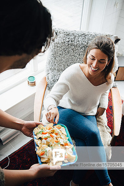Smiling woman taking snacks from friend during party at home