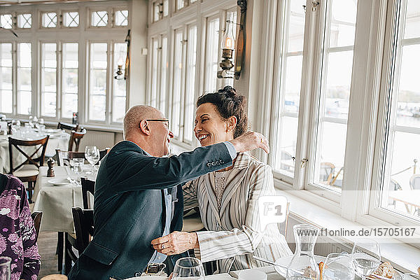 Senior man embracing woman while sitting in restaurant