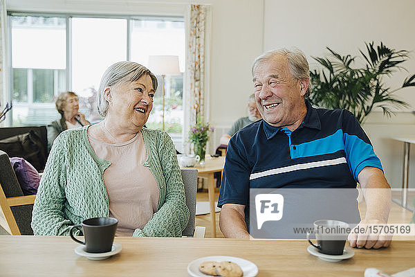 Smiling elderly senior friends talking while sitting at dining table in nursing home