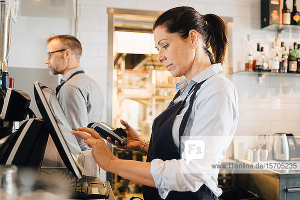 Owner using computer while holding credit card reader in restaurant