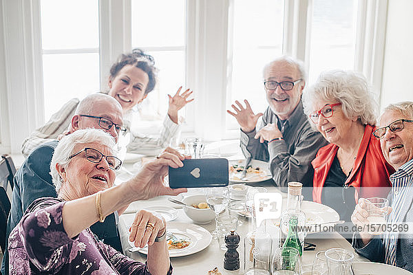 Frau klickt Foto von älteren Freunden per Smartphone an  während sie im Restaurant sitzt